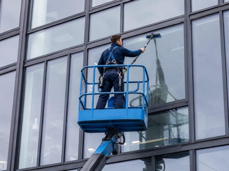 Mitarbeiter im Korb einer Hubarbeitsbühne reinigt die Glasfläche einer Bürofassade in großer Höhe