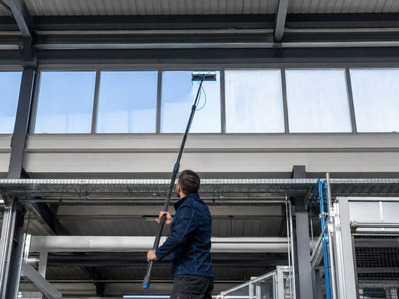 Mitarbeiter reinigt ein Hallenlichtband von innen mit einer Teleskopstange